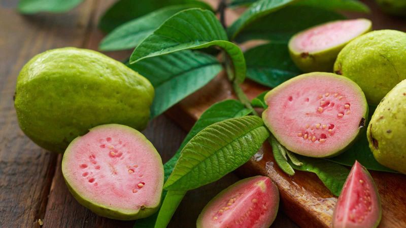 Meia goiaba rosa suculenta em close-up com folhas verdes, destacando os benefícios para a imunidade, perfeita para ilustrar conteúdos de saúde e nutrição.